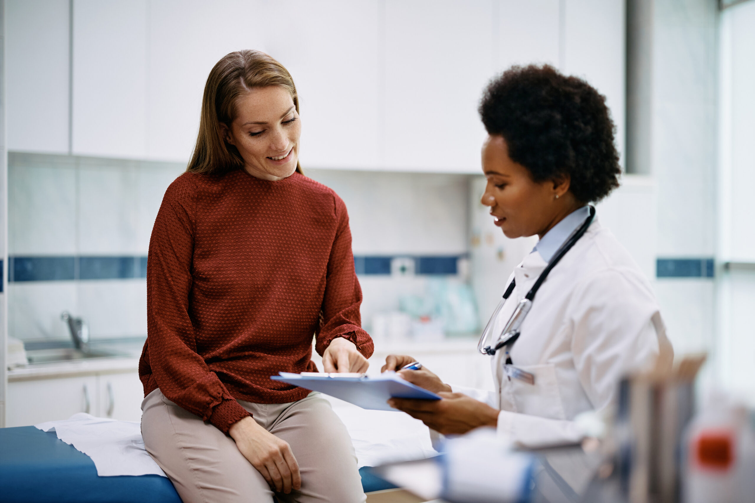 Doctor and her patient analysing medical report after examination in the hospital. Focus is on patient.
