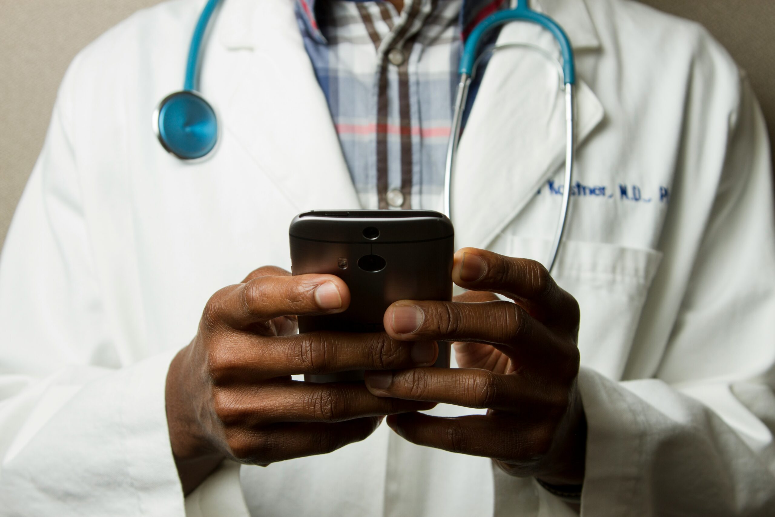 A medical expert with a stethoscope around his neck holds a mobile phone . Implying that the phone is used as part of his practise